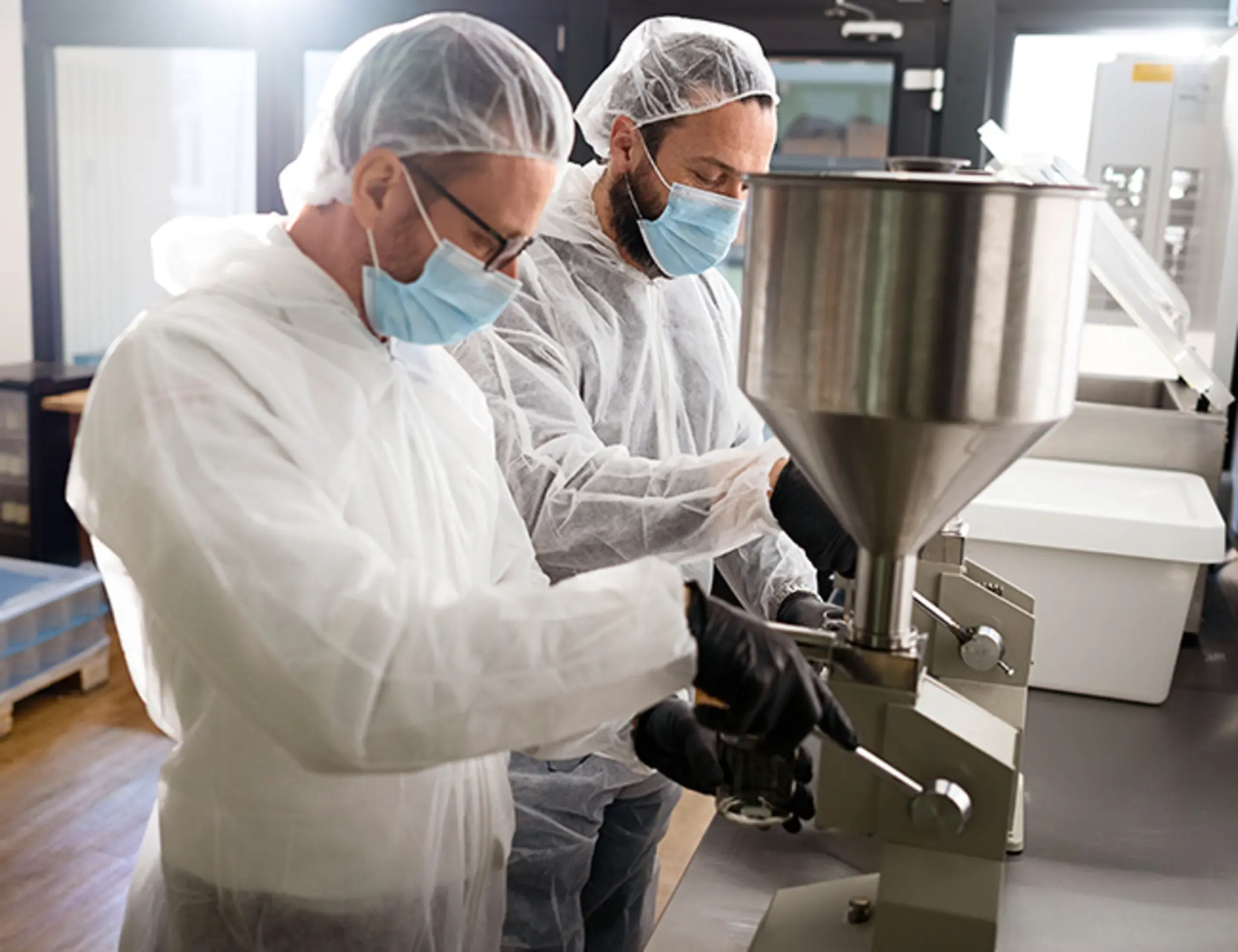 Robert Buljat und Andre Becker mit Mundschutz und Haarnetz in der Großküche. Gemeinsam füllen sie Aioli in Gläser ab.