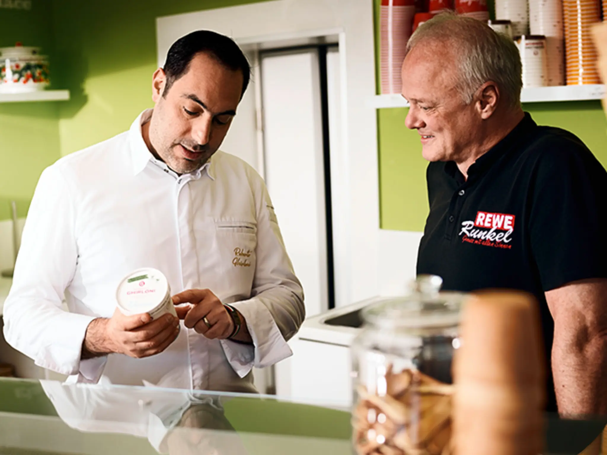 Roberto Ghirloni zeigt Frank Runkel einen Becher Eis.