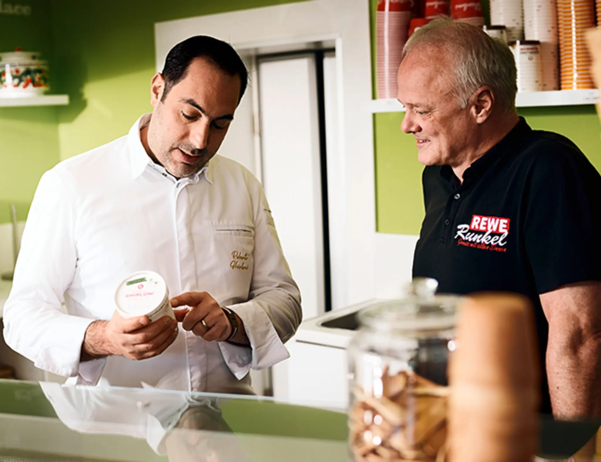 Roberto Ghirloni zeigt Frank Runkel einen Becher Eis.