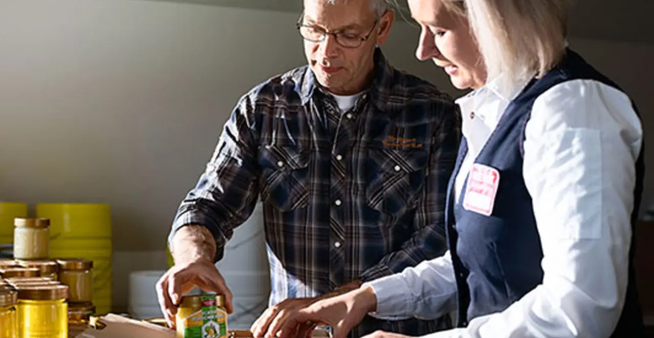 Imker Jan Fischer und REWE Kauffrau Olga Berg verpacken regionale Honiggläser in Pappkartons. 