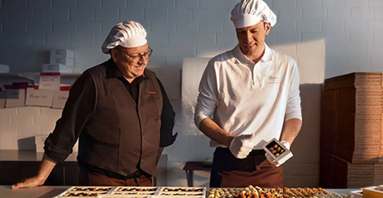 REWE Kaufmann Christoph Steverding schaut Pralinen-Produzent Lukas Große-Bölting in der Manufaktur-Küche über die Schulter.