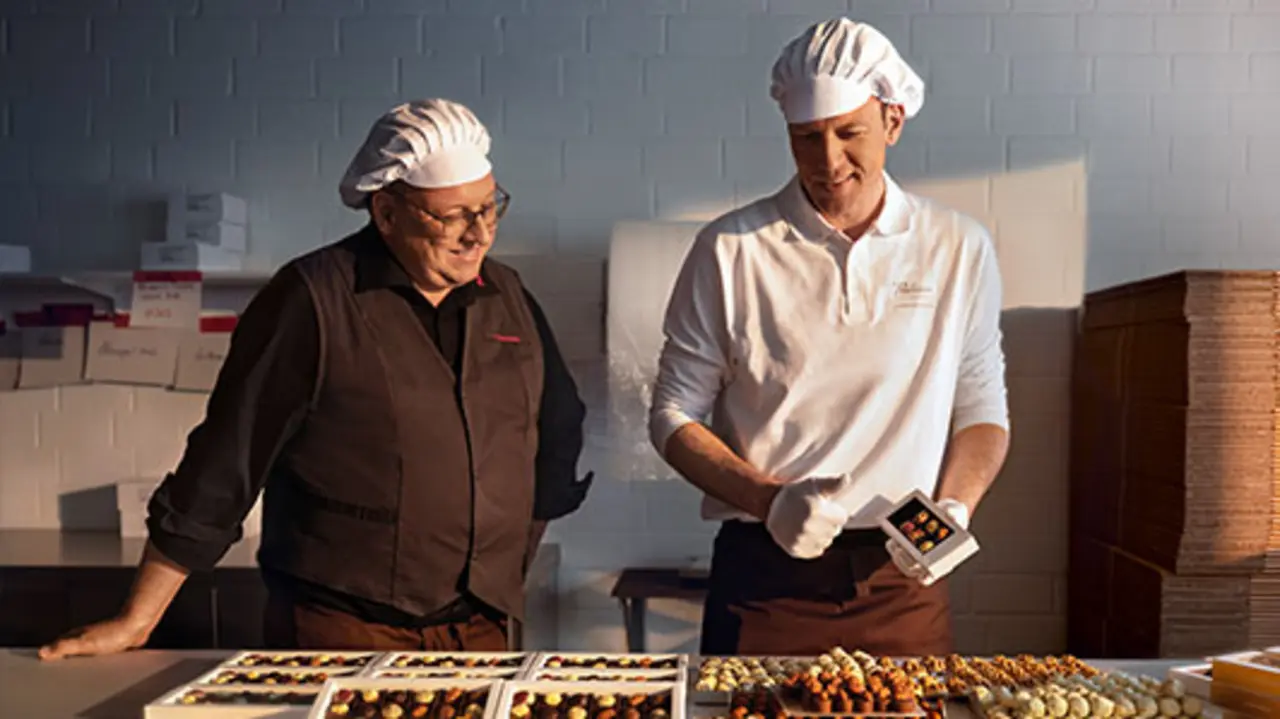 REWE Kaufmann Christoph Steverding schaut Pralinen-Produzent Lukas Große-Bölting in der Manufaktur-Küche über die Schulter.