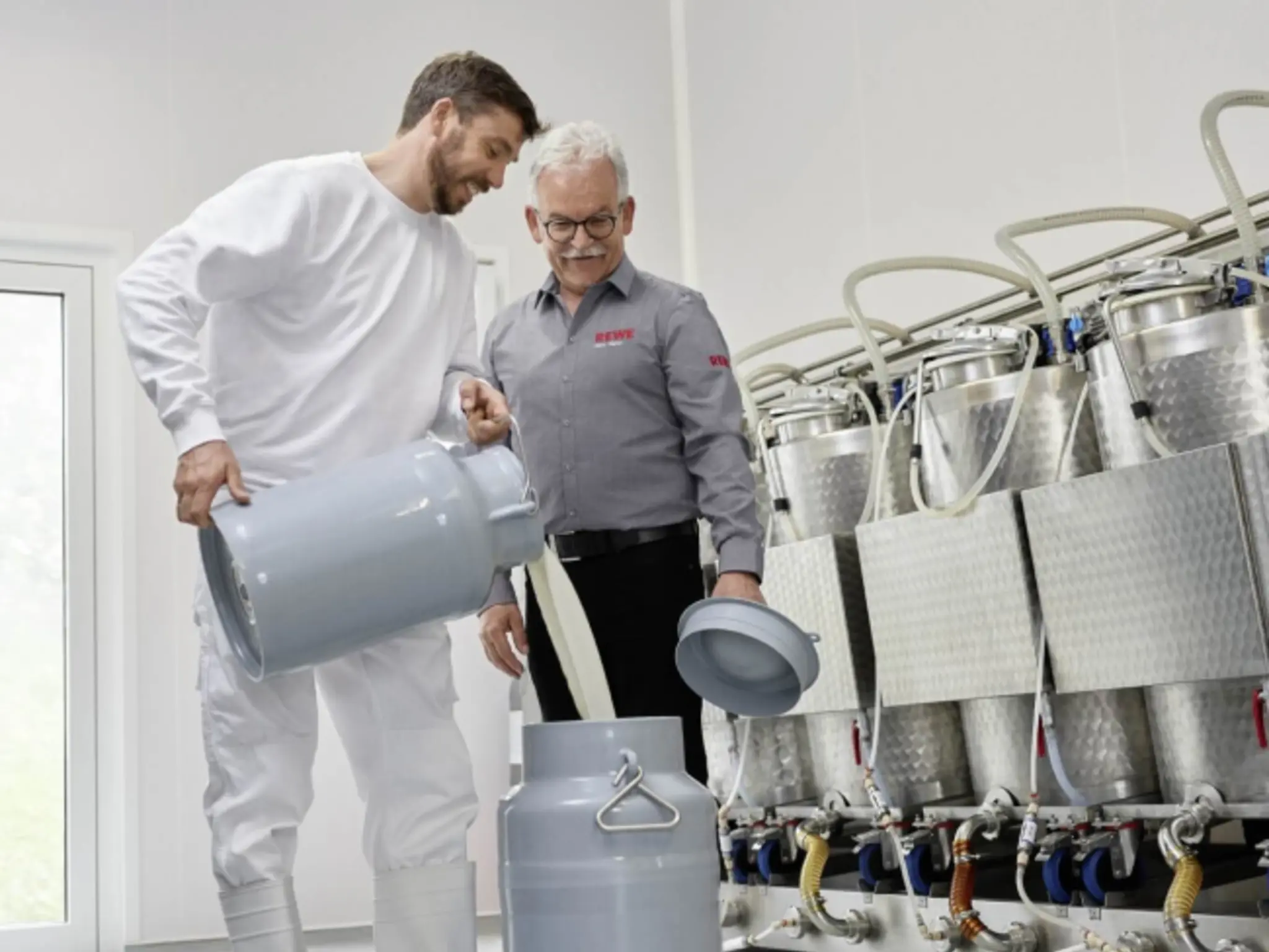 Michael Müller füllt frische Milch in eine große Kanne. Rainer Hahn hält den Deckel.