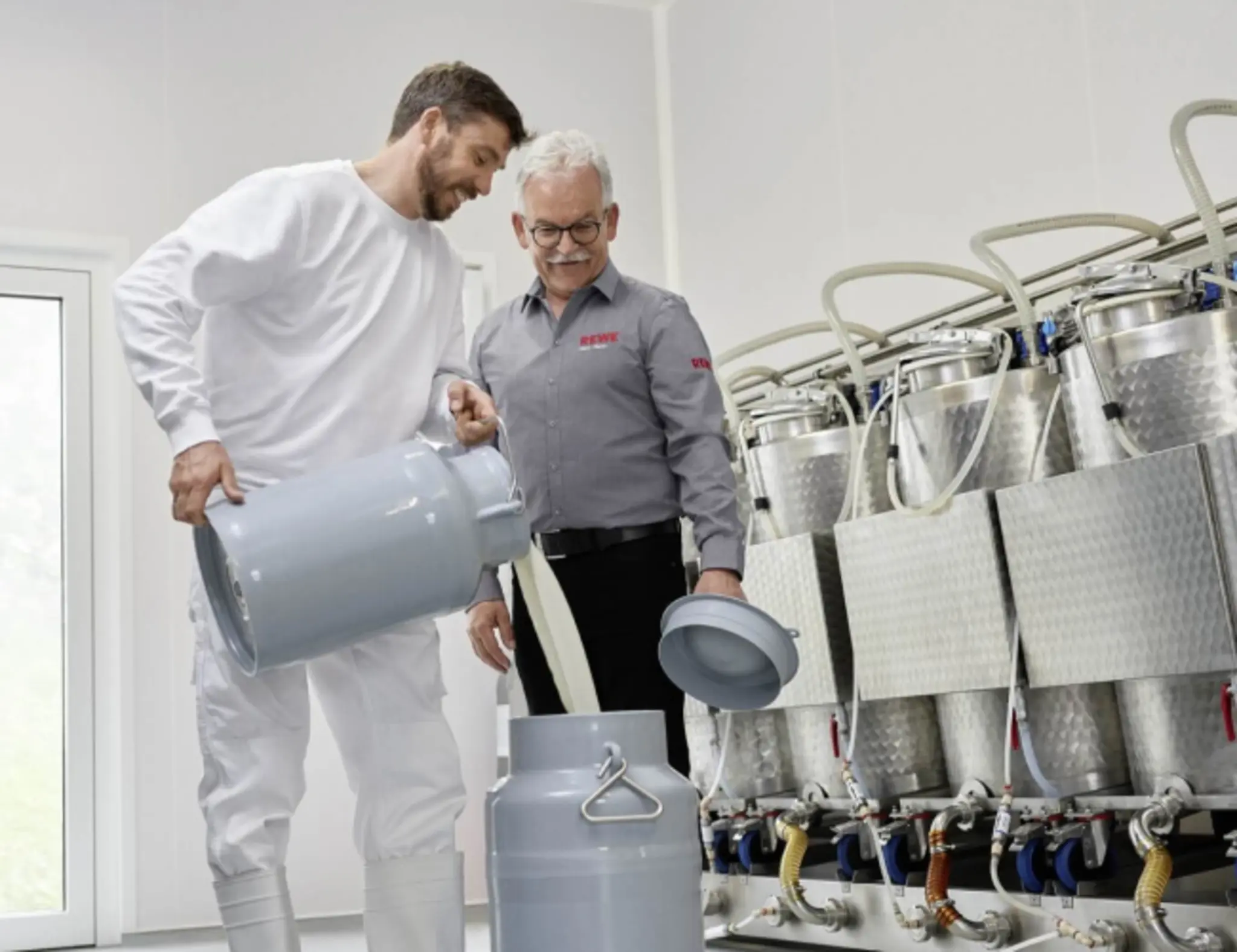 Michael Müller füllt frische Milch in eine große Kanne. Rainer Hahn hält den Deckel.