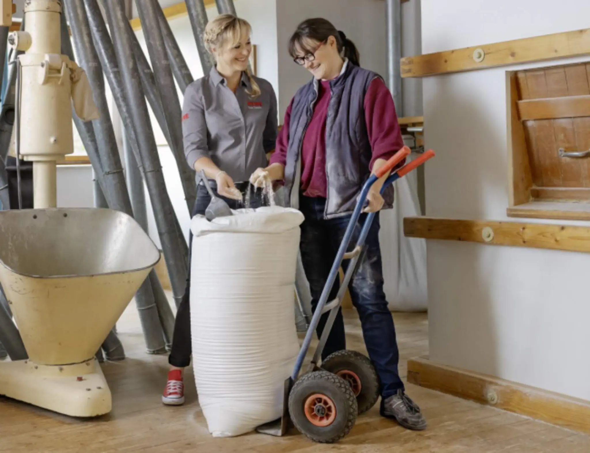 Susann Daubitz und Petra Schuster in der Schustermühle. Sie stehen vor einem großen Mehlsack. Petra Schuster lässt sich Mehl durch die Finger rieseln.
