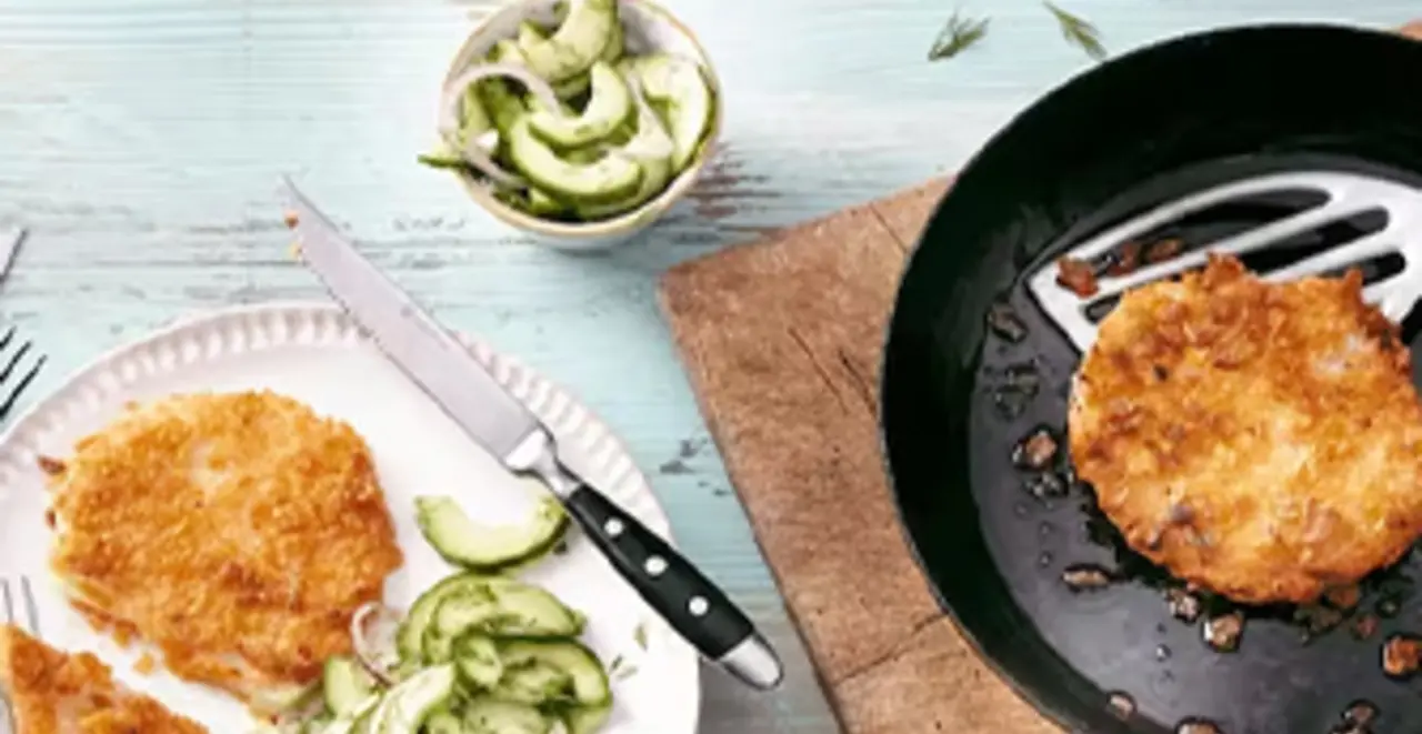 Auf zwei Tellern sind schon Kohlrabi-Schnitzel mit Gurkensalat angerichtet. Ein drittes Schnitzel liegt noch in der Pfanne.