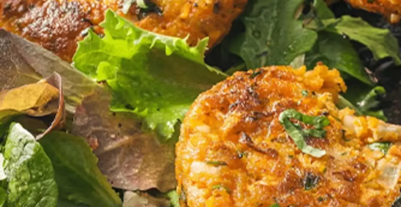 Auf einem Teller sind drei Möhren-Feta-Bratlinge mit frischem Salat angerichtet.