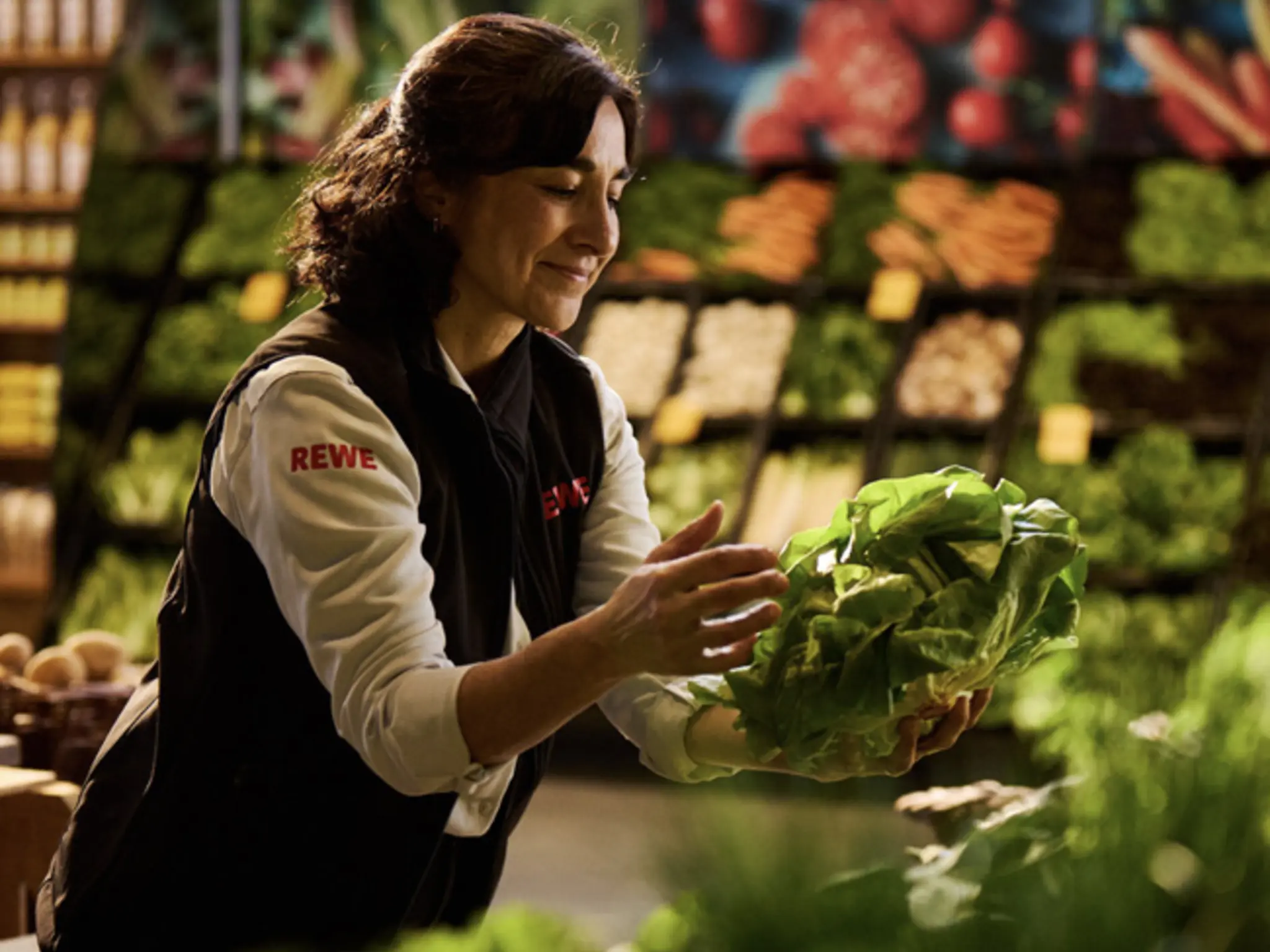REWE-Mitarbeiterin legt Salat in Gemüseabteilung