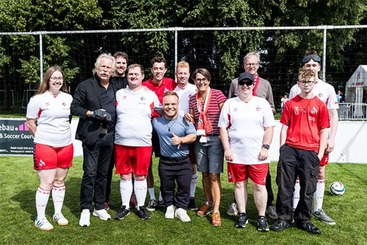 Gruppe von Fußballspielern in rot-weißen Trikots und Begleitpersonen posiert gemeinsam auf einem Fußballplatz vor einem Tor bei sonnigem Wetter. Copyright: Jannik Czauderna (Alt-Tag 9)