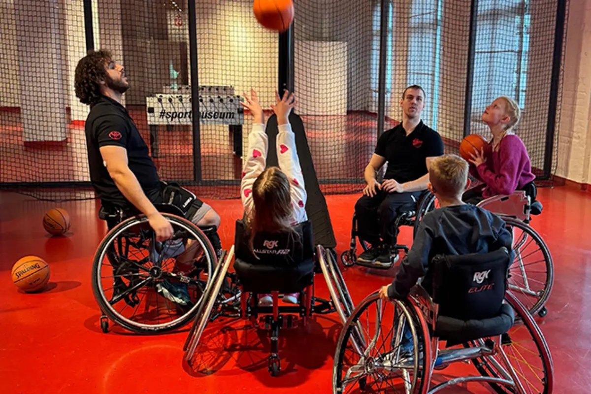 Mehrere Kinder und ein Trainer im Rollstuhl spielen gemeinsam Basketball. 