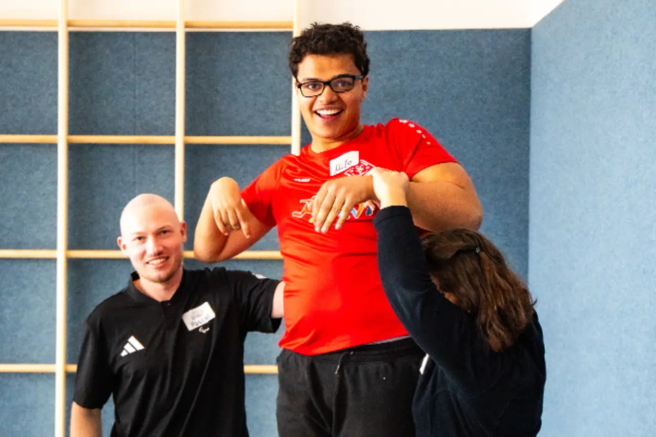 Beim Besuch des Inklusionsmobils trainiert ein Jugendlicher mit Behinderung in der Turnhalle des SC Vilkerath. Zwei Trainer:innen unterstützen ihn.