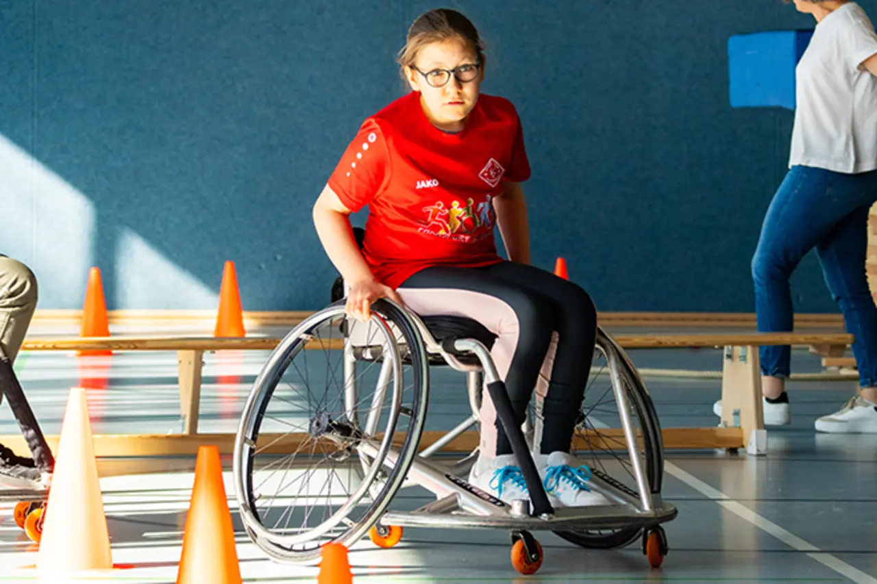 Die Turnhalle des SC Vilkerath beim Besuch des Inklusionsmobils. Eine Jugendliche fährt im Rollstuhl einen Geschicklichkeitsparcours.