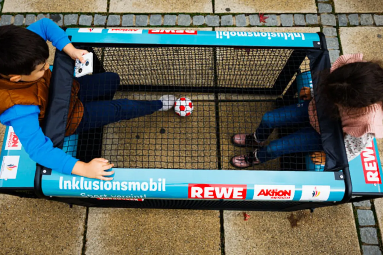 Zwei Kinder spielen Fußball an einem inklusiven Sportgerät.