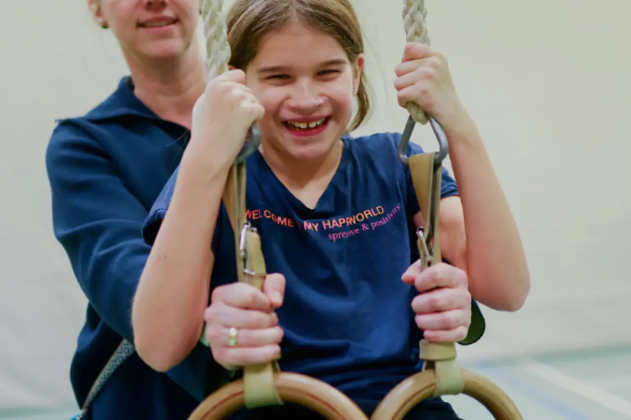 In einer Turnhalle. Zwei Kinder spielen mit einem Gymnastikball.