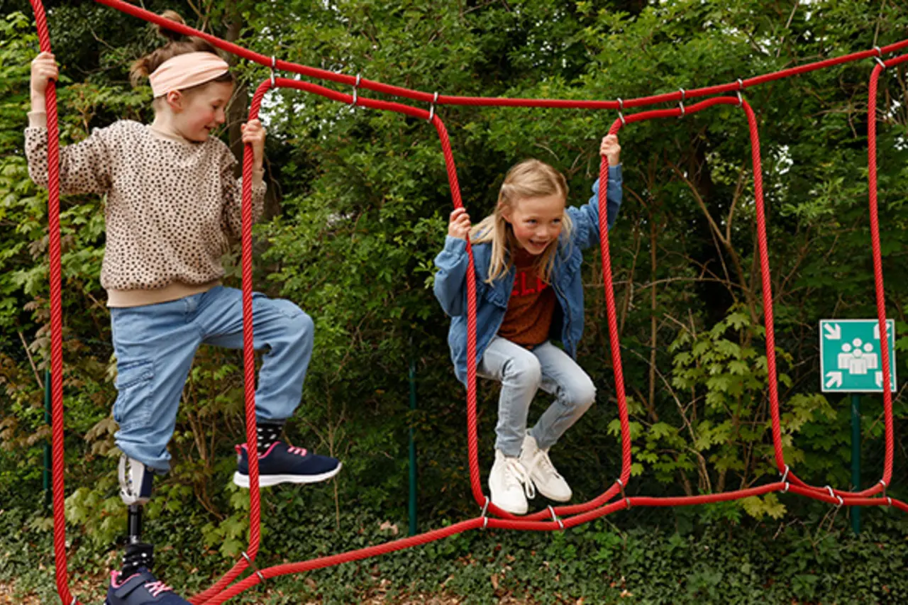 Ein Kind mit Beinprothese auf einem inklusiven Klettergerüst. 