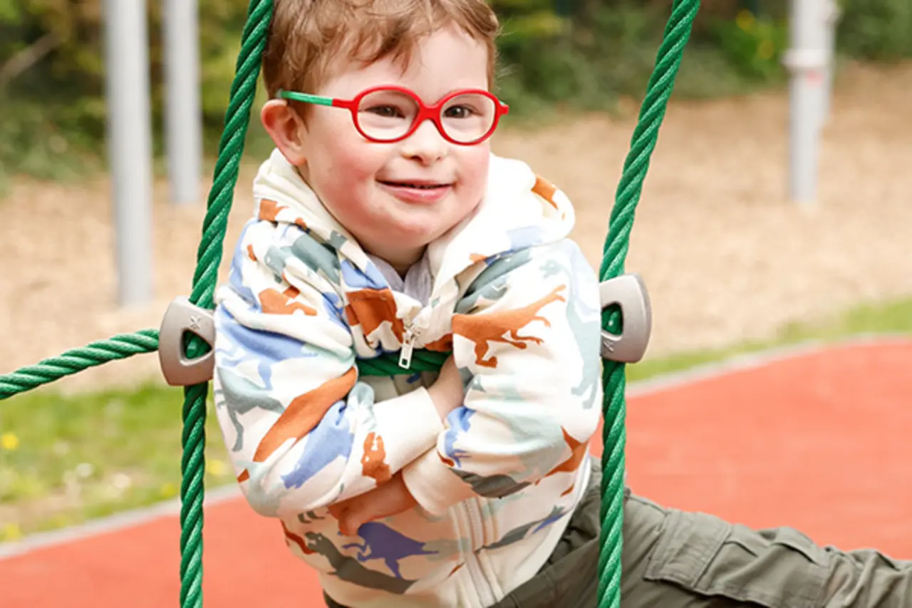 Ein Kind mit Behinderung schaut durch die Stufen eines inklusiven Klettergerüstes. 