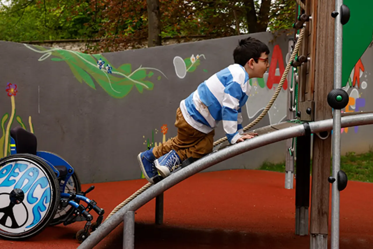 Ein Kind klettert aus dem Rollstuhl direkt auf ein inklusives Spielgerät. 