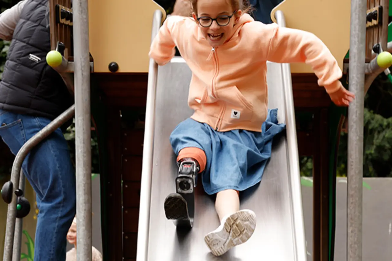 Ein Kind mit Beinprothese lacht auf der inklusiven Rutsche.  