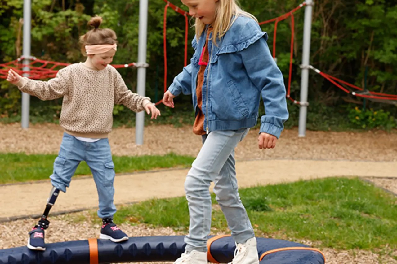 Zwei Kinder mit und ohne Behinderung balancieren auf einem inklusiven Spielgerät. 