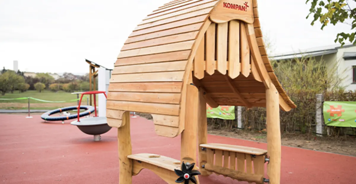 Ein inklusiver Spielplatz mit rotem Gummiboden. Im Vordergrund steht ein inklusives Spielgerät.