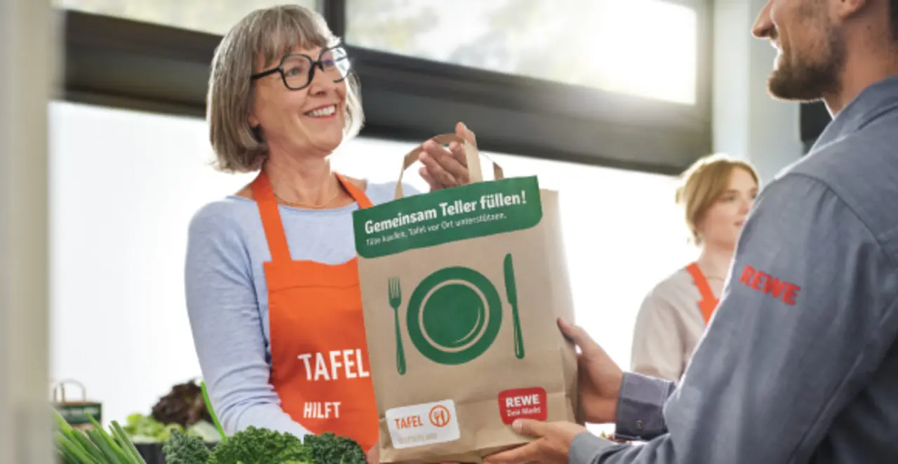 Eine Helferin der Tafel gibt einer anderen Person eine Tüte mit Lebensmitteln.