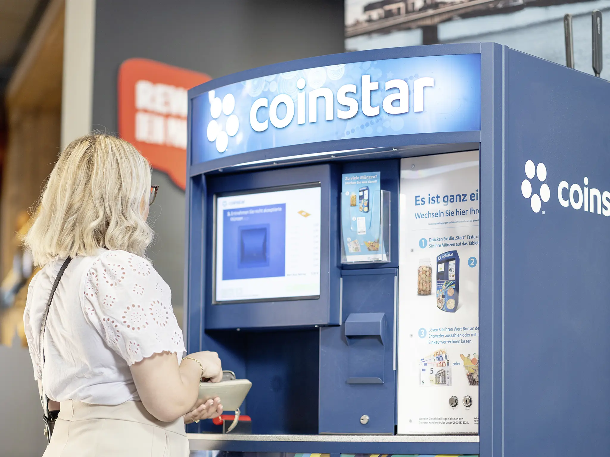 Eine REWE Kundin spendet ihr Kleingeld an einem Coinstar Automaten.