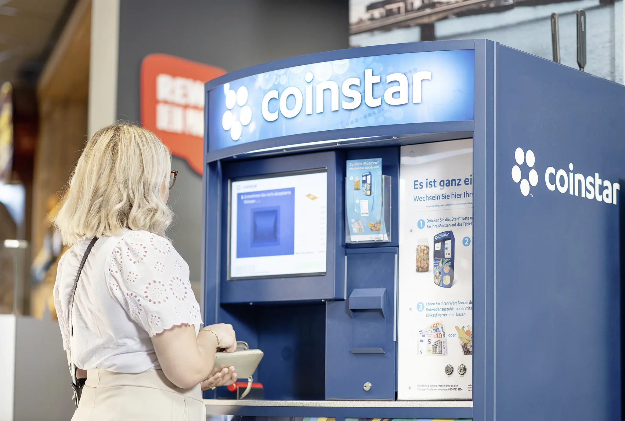 Eine REWE Kundin spendet ihr Kleingeld an einem Coinstar Automaten.