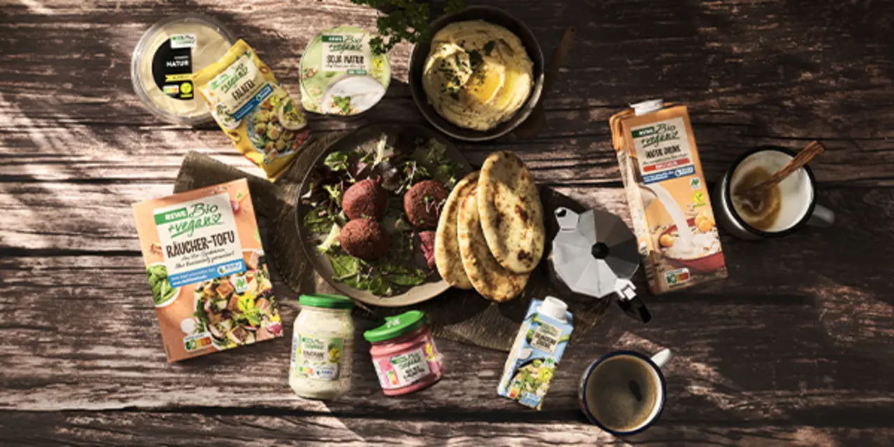 Verschiedene REWE Bio und REWE Bio + vegan Produkte liegen auf einem rustikalen Holztisch. Mit dem Kauf unterstützt du den NABU-Klimafonds. 