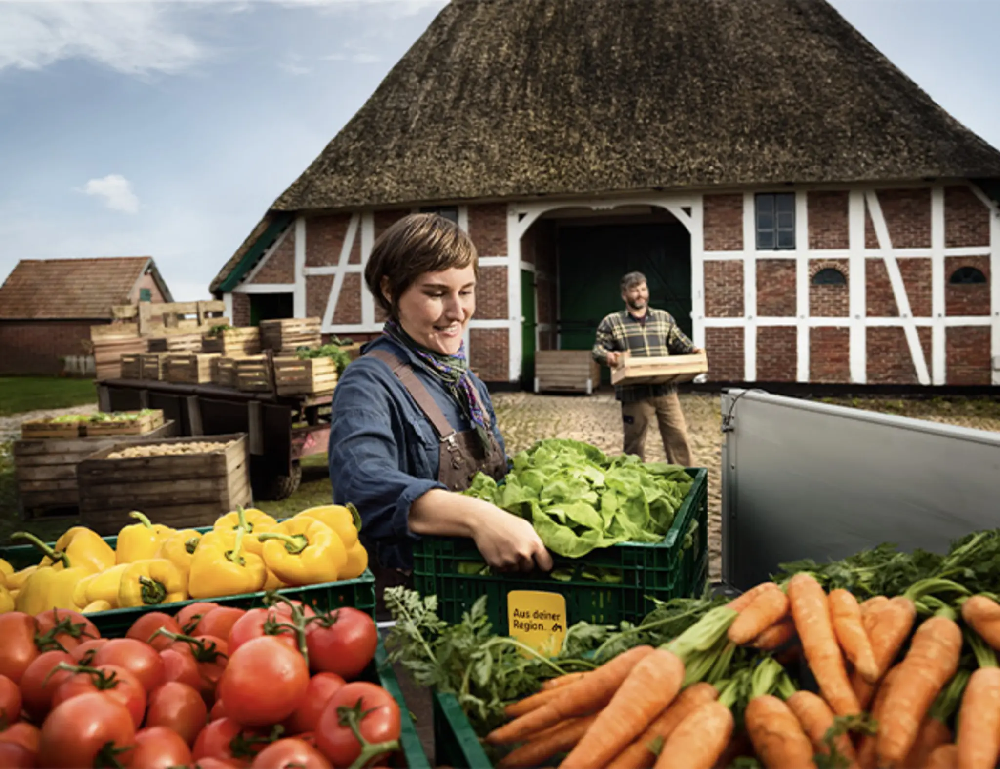 Regionale Erzeuger:innern laden Obst und Gemüse auf einen Anhänger. Zwischen den Produkten steckt das gelbe Schildchen mit dem Schriftzug „Aus deiner Region“, das du auch im Markt findest. 