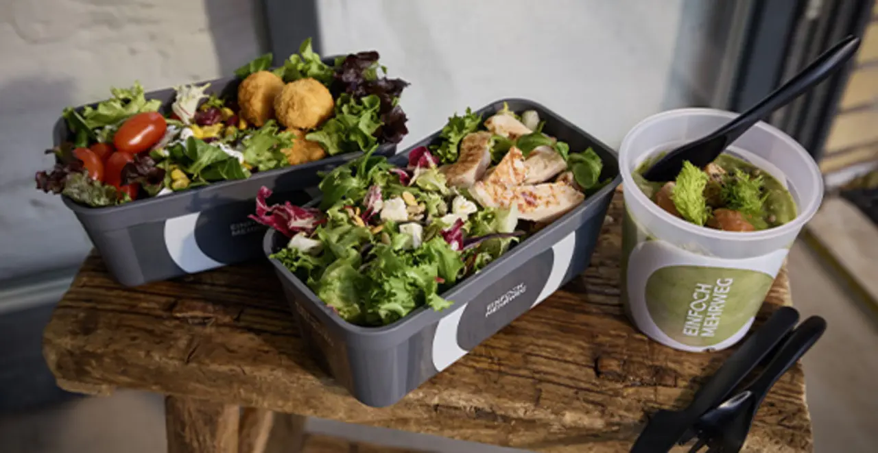 Mehrere Mehrweg-Pfandbehälter mit frischen Salaten und Suppen. 