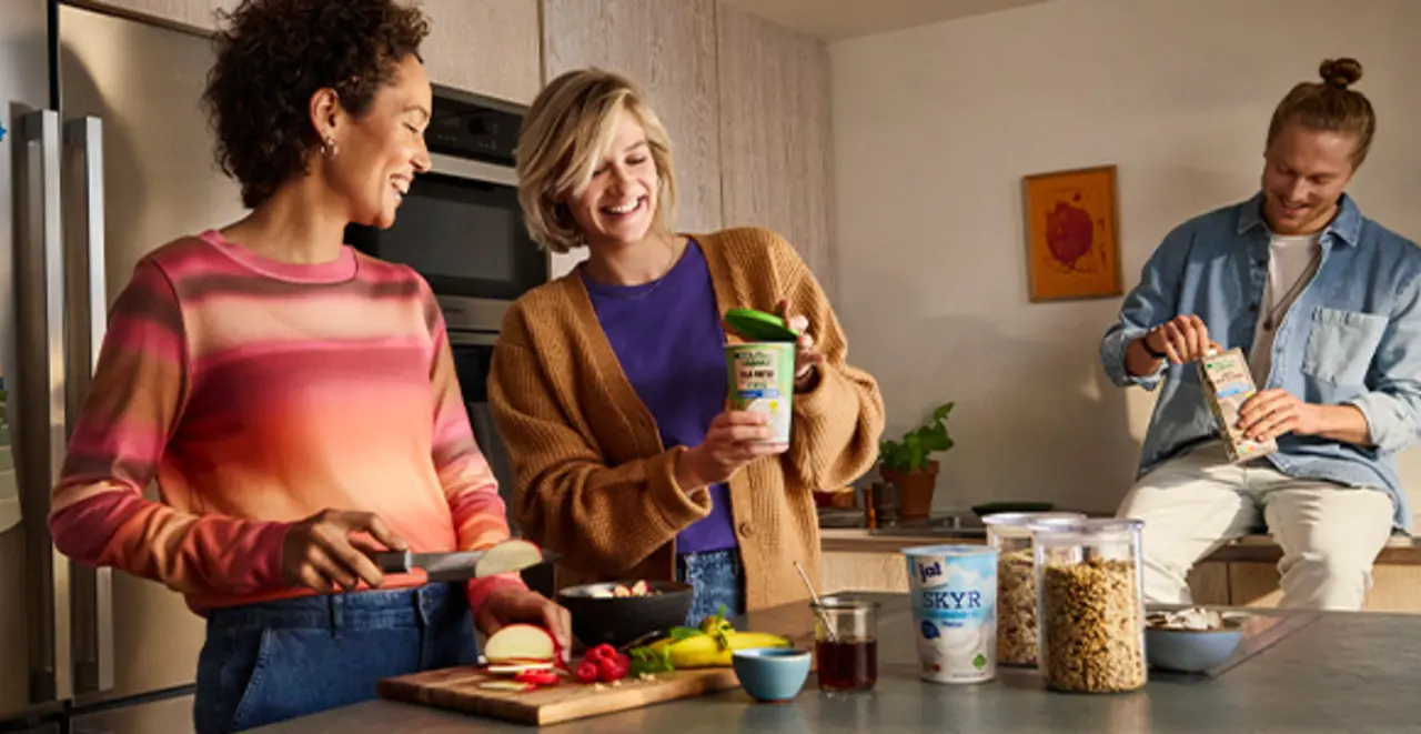 Drei Menschen zuhause am Küchentresen. Auf der Arbeitsfläche stehen verschiedene REWE Produkte mit verbesserten Verpackungen.