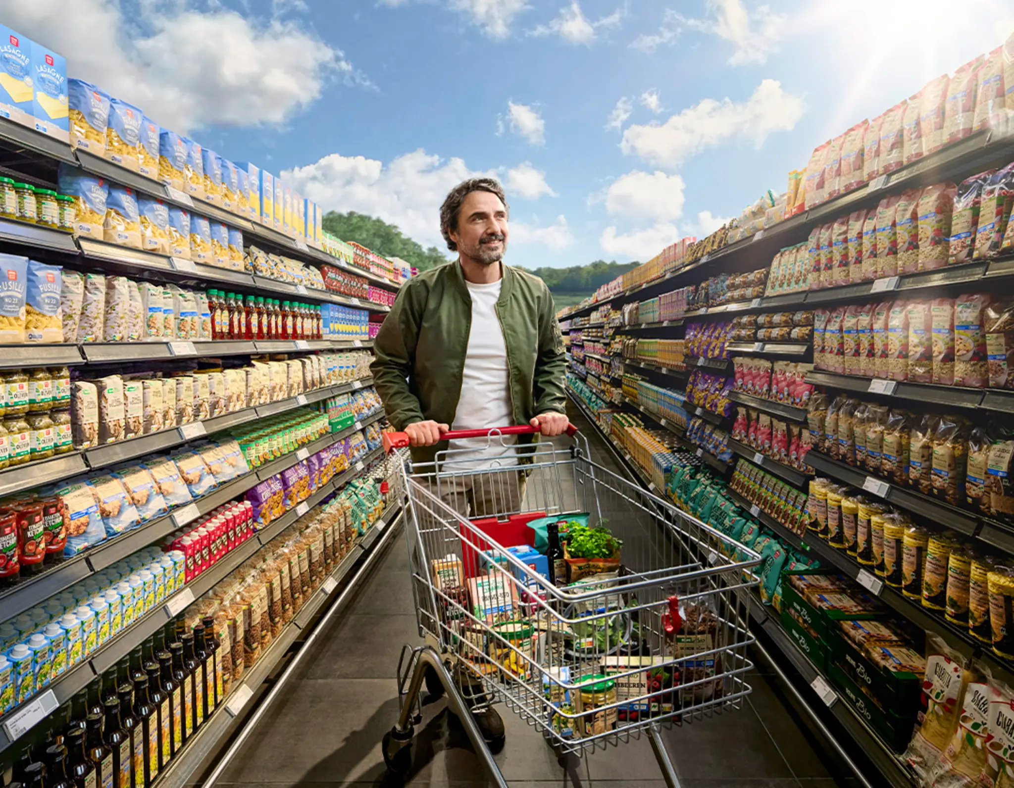 Hinter einer scheinbar endlosen Regalreihe beginnt eine Wiese mit einem Waldstück. Ein REWE Kunde betrachtet die riesige Auswahl an nachhaltigeren Produkten. 