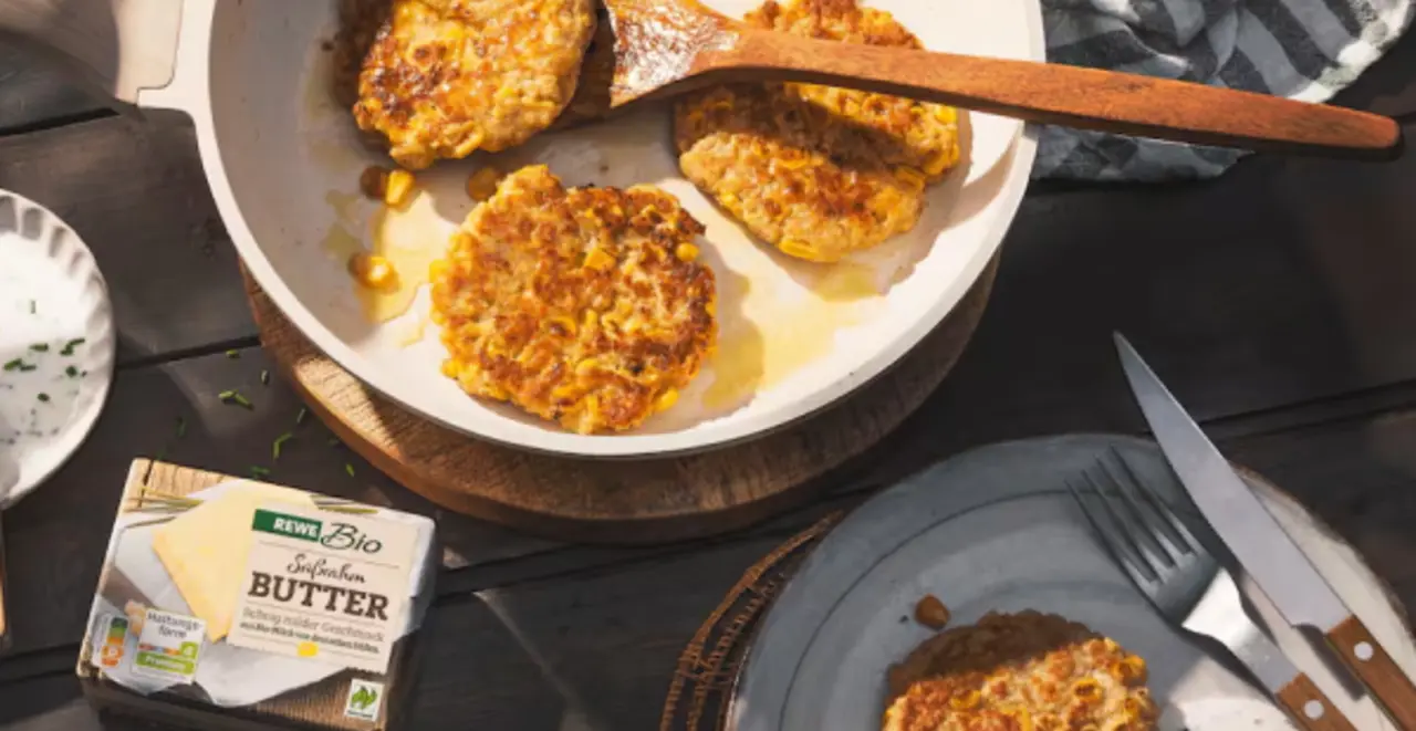 Ein Teller mit Bratlingen und Joghurt-Dip. Oberhalb steht eine Pfanne mit weiteren Bratlingen. Links eine Schüssel Joghurt Dip und eine Paclung REWE Bio Butter.  