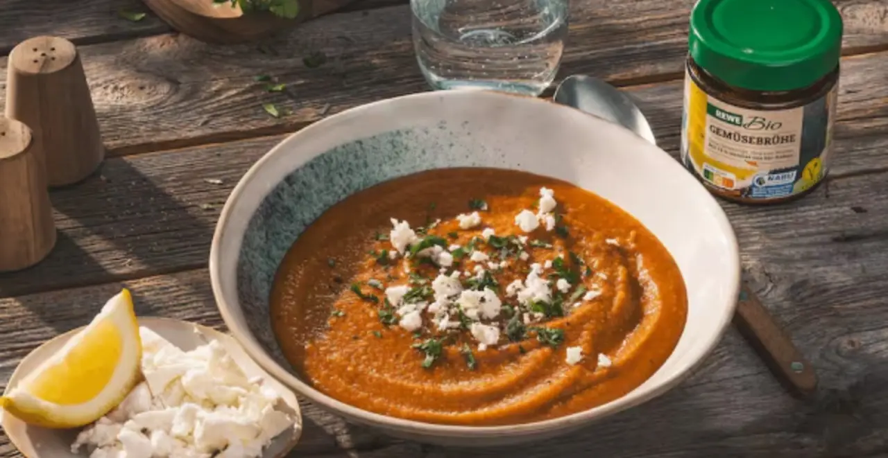 Ein Teller Linsensuppe mit Feta. Links davon ein kleiner Teller mit Feta und einem Stück Zitrone, rechts ein Glas REWE Bio Gemüsebrühe.  