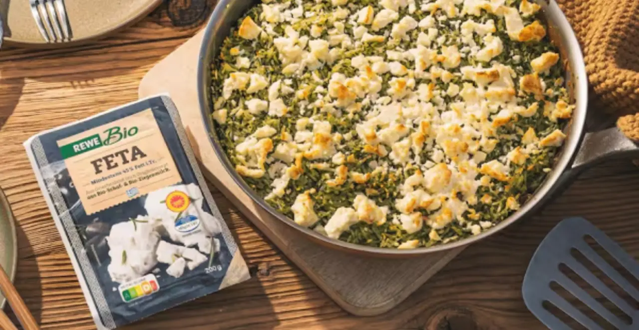 Eine Pfanne mit gebackenem Spinat und Feta. Links daneben eine Packung REWE Bio Feta.