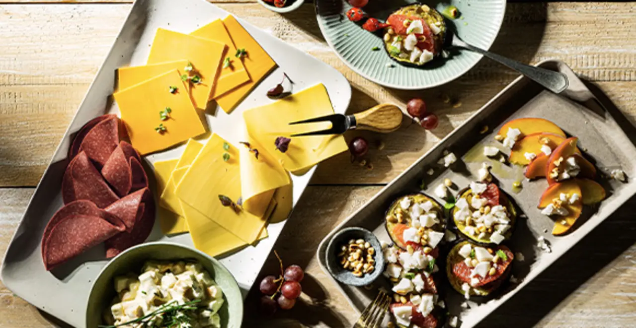 Auf einem gedeckten Tisch steht eine Platte mit pflanzlichem Käse und Aufschnitt. 