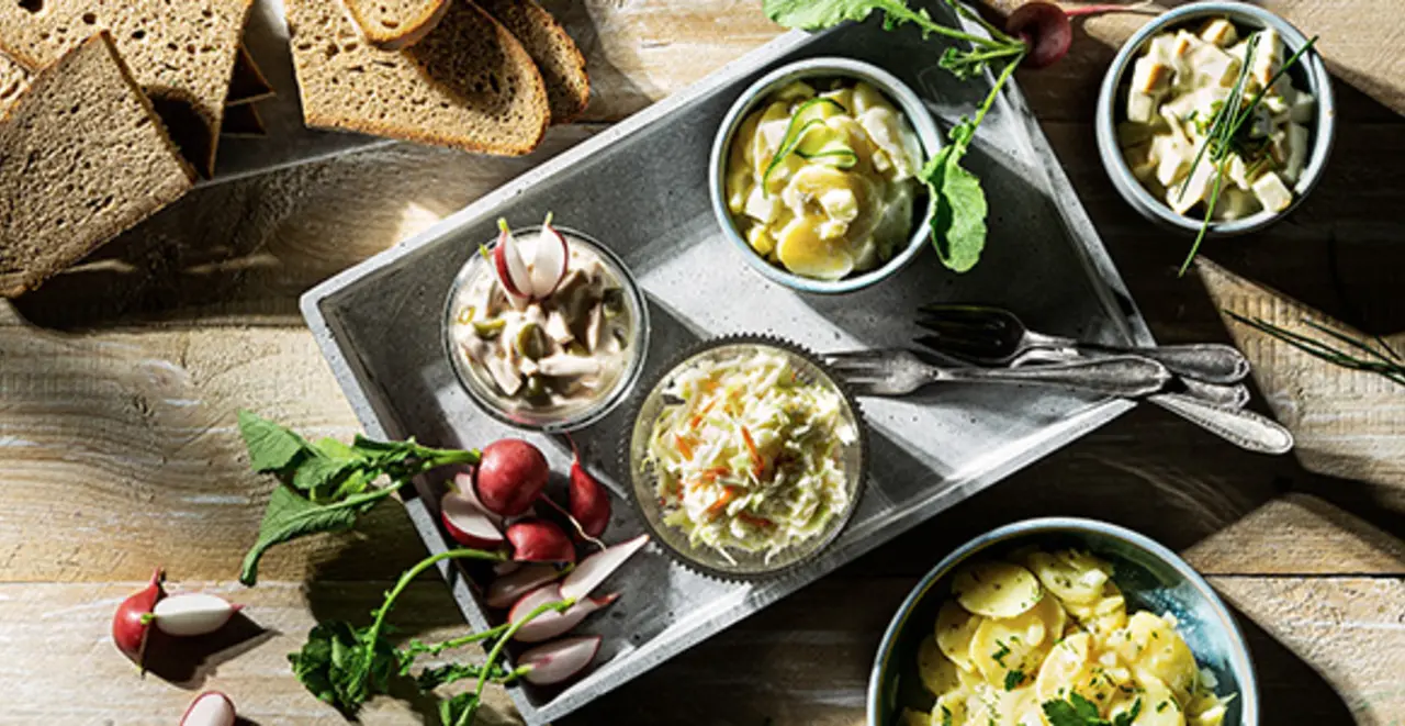 Auf einem gedeckten Holztisch stehen verschiedene pflanzliche Salate.